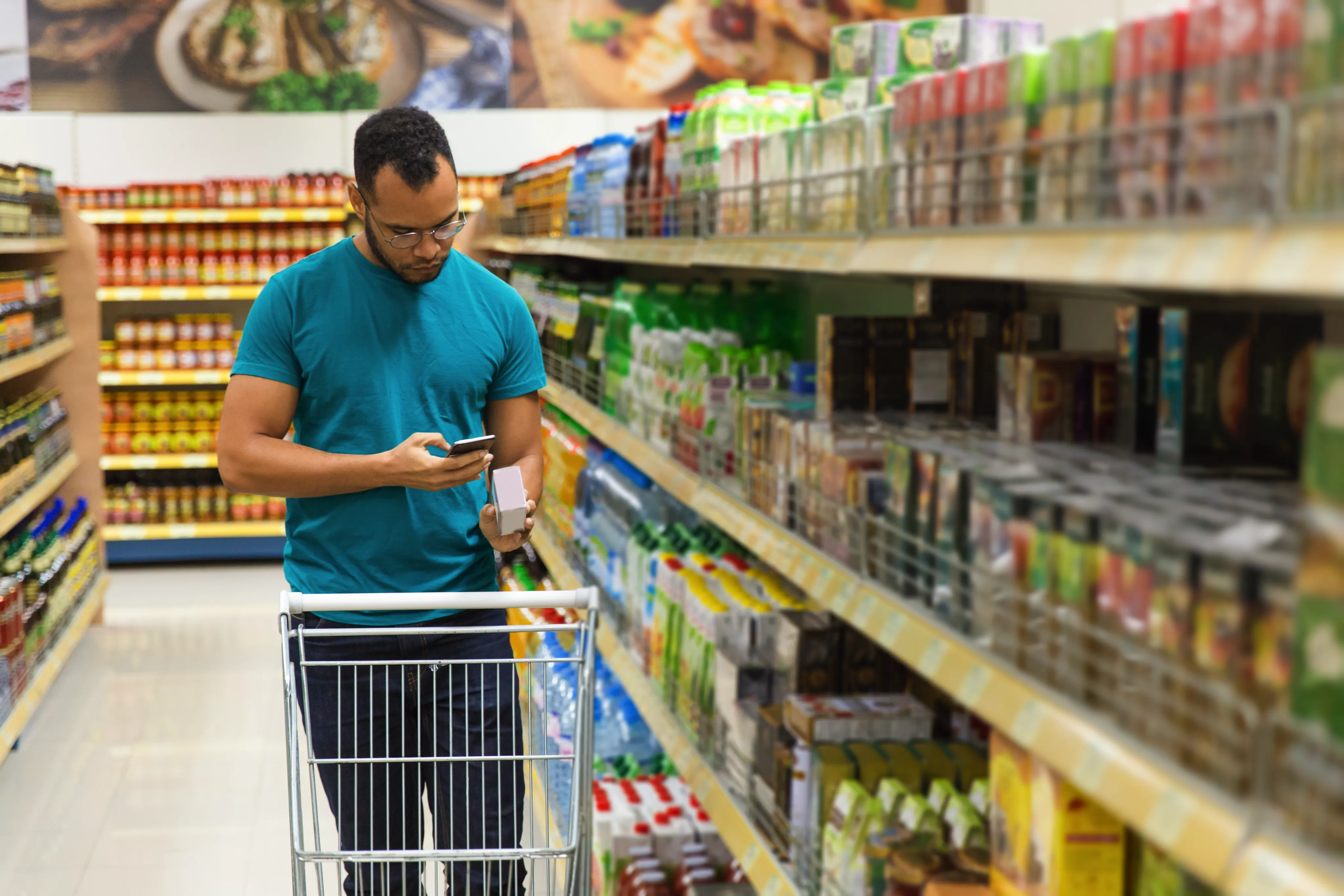 Shopper with a trolley checking a product on his phone